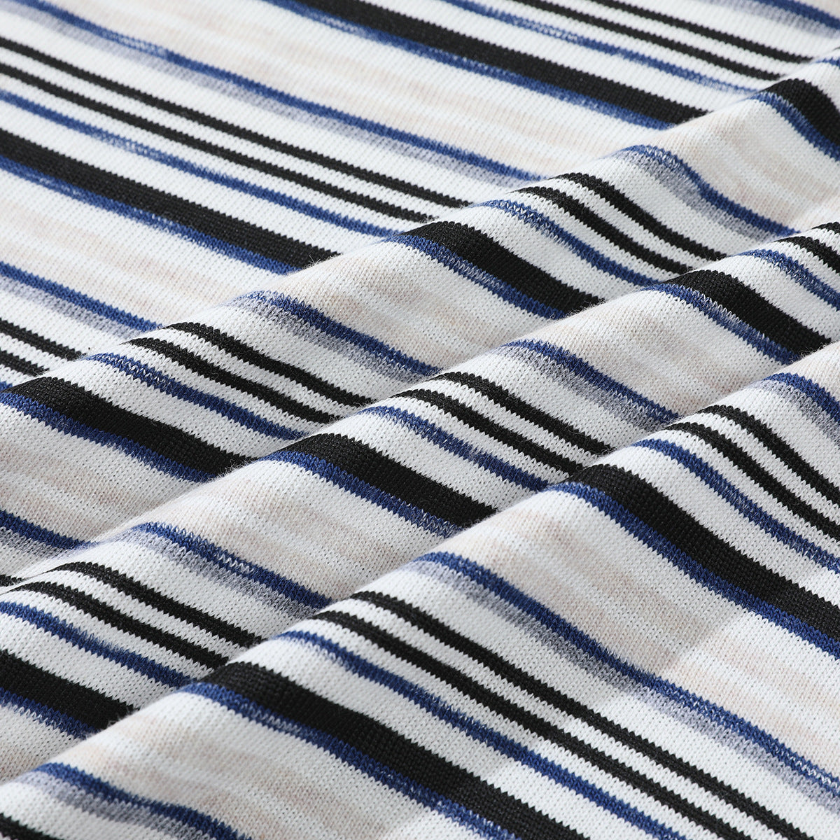 Close-up of white striped knit fabric arranged in soft folds, showing black, navy, and gray lines.