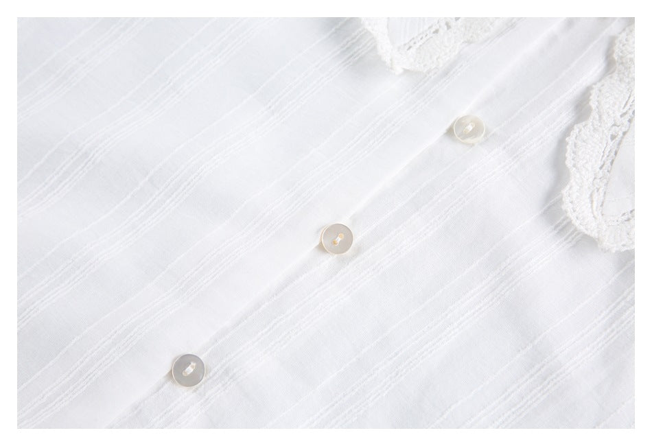 Close-up of white striped-texture garment fabric with translucent buttons and a crocheted lace edge.