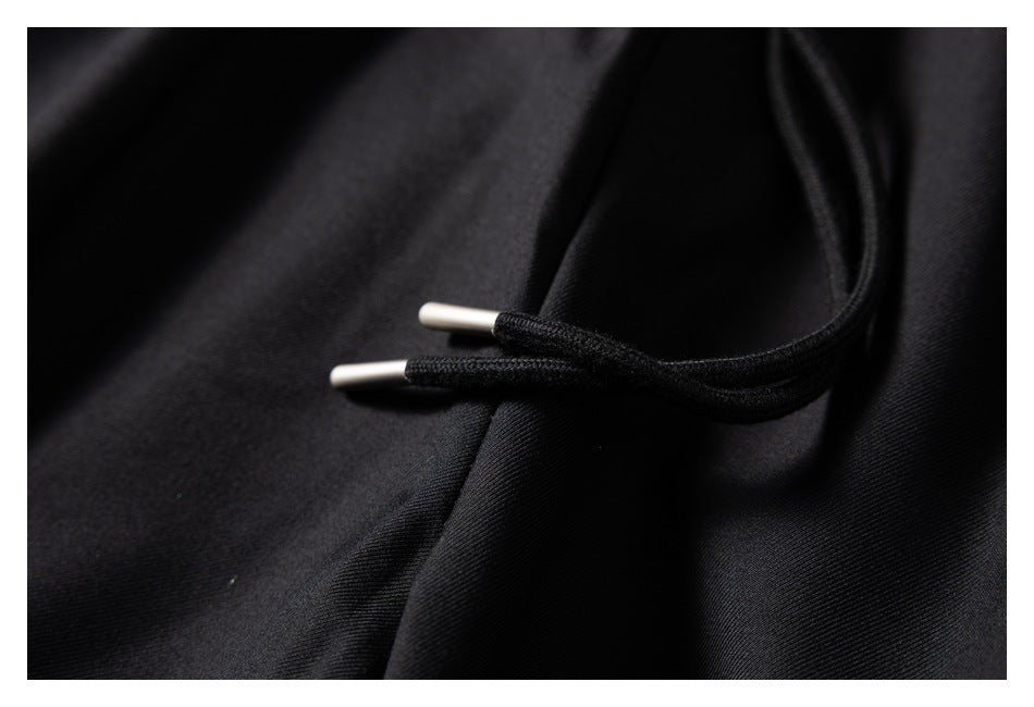 Close-up of black garment fabric with a black drawcord and silver-colored cord tips.