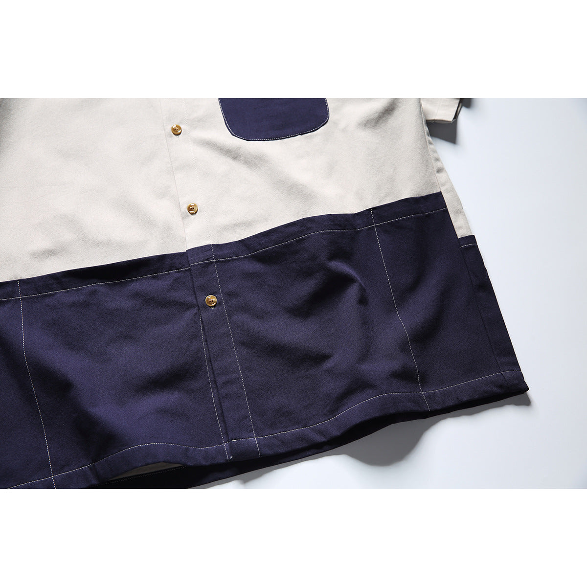 Close-up of the shirt's navy lower front panel, showing tan buttons, contrast stitching, and the hem.
