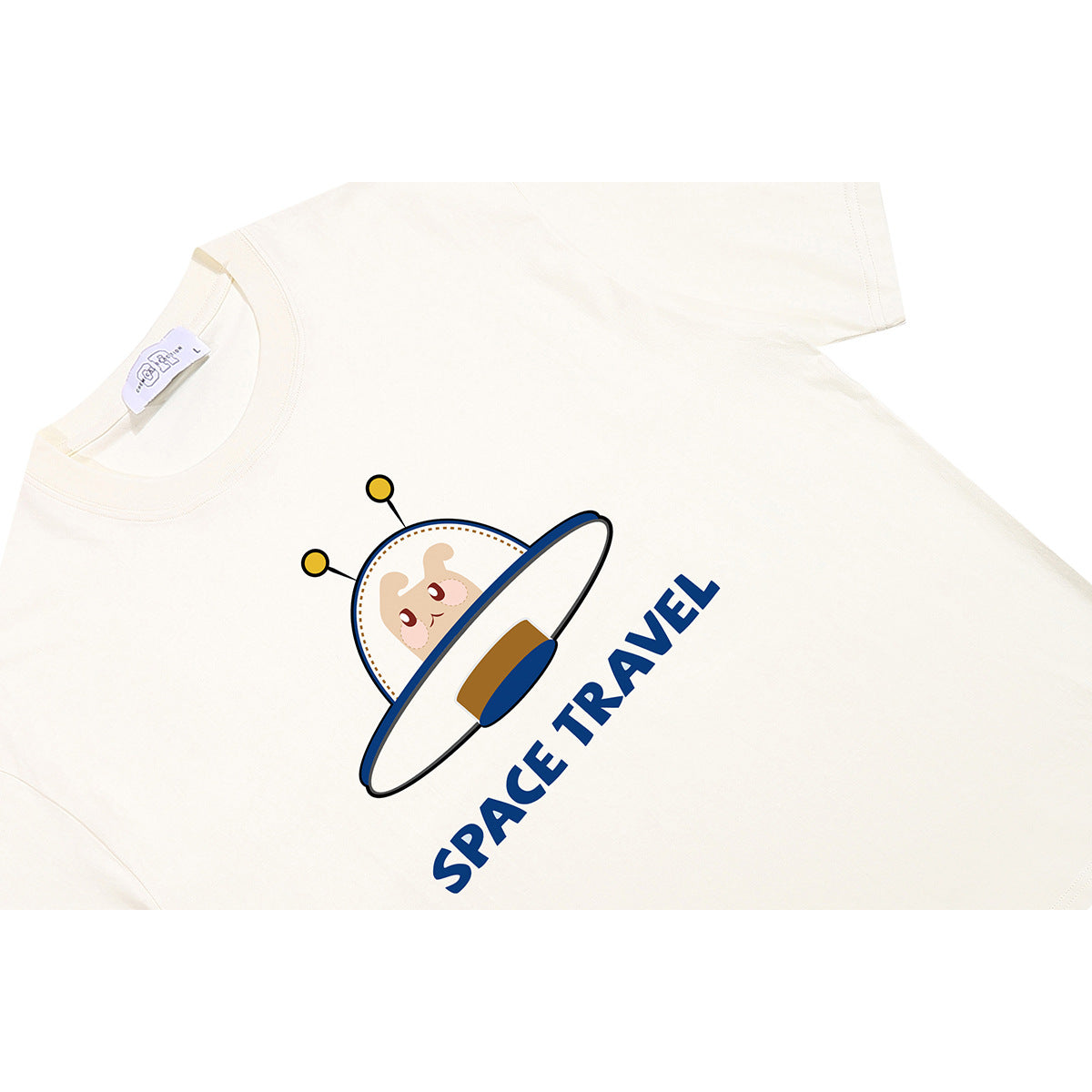 Angled flat lay of an ivory T-shirt with a cartoon UFO and blue “SPACE TRAVEL” lettering.