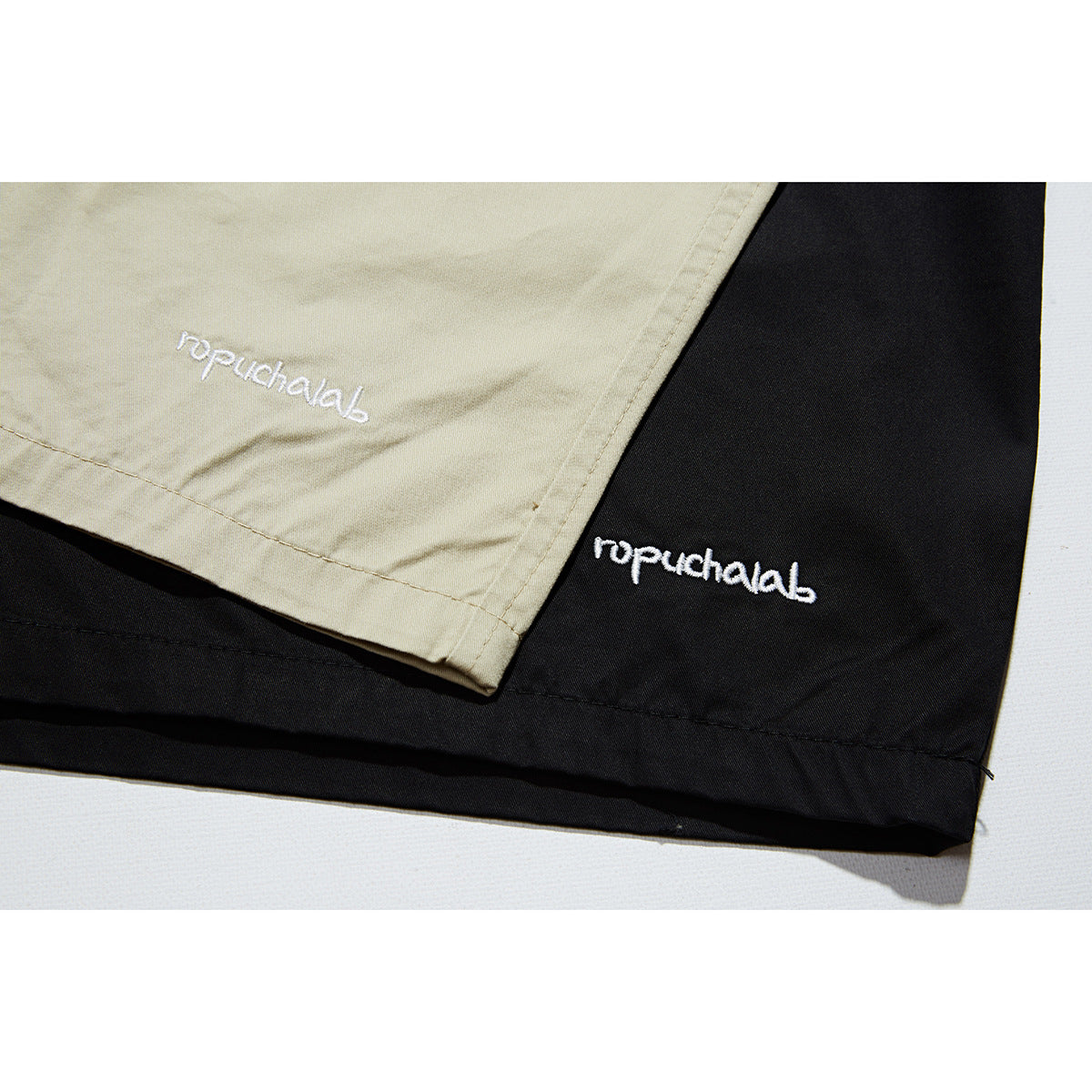 Close-up of white script embroidery near the hems of beige and black shorts.