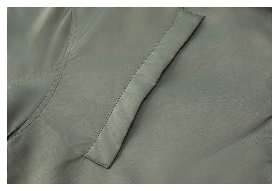 Close-up of a narrow fabric flap pocket on an olive-gray garment.
