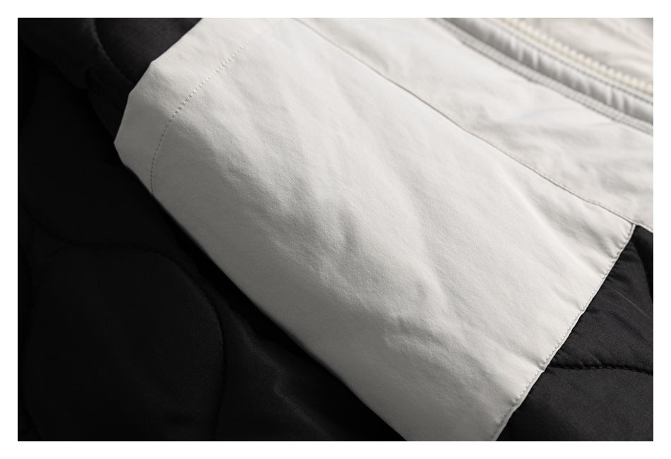 Close-up of a pale gray fabric panel over black quilted garment fabric, showing stitched seams.
