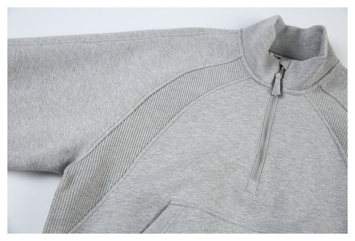 Angled close-up of the light gray sweatshirt’s front zipper, stand collar, ribbed side panel, and pocket edge.