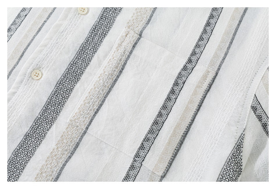 Close-up of a white shirt with vertical black and beige woven stripes, two buttons, and a chest pocket.