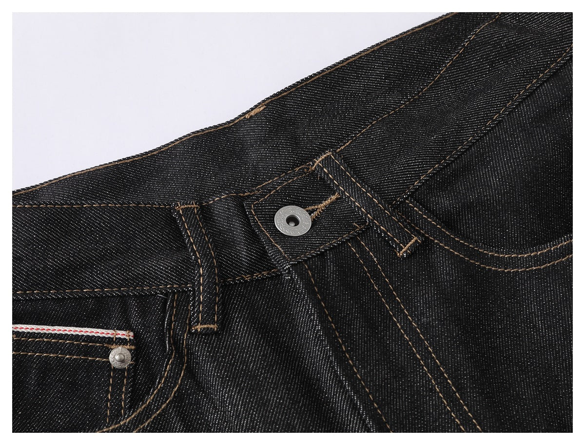 Angled close-up of black denim jeans showing the waistband, belt loops, front button and pocket stitching.