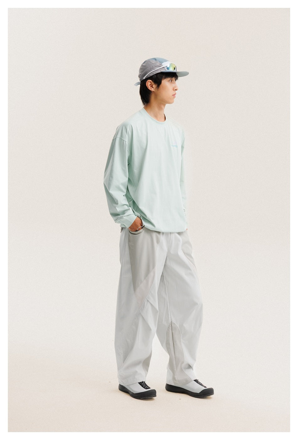 Side view of a man wearing a pale mint long-sleeve shirt, loose light-gray trousers, and a gray cap.