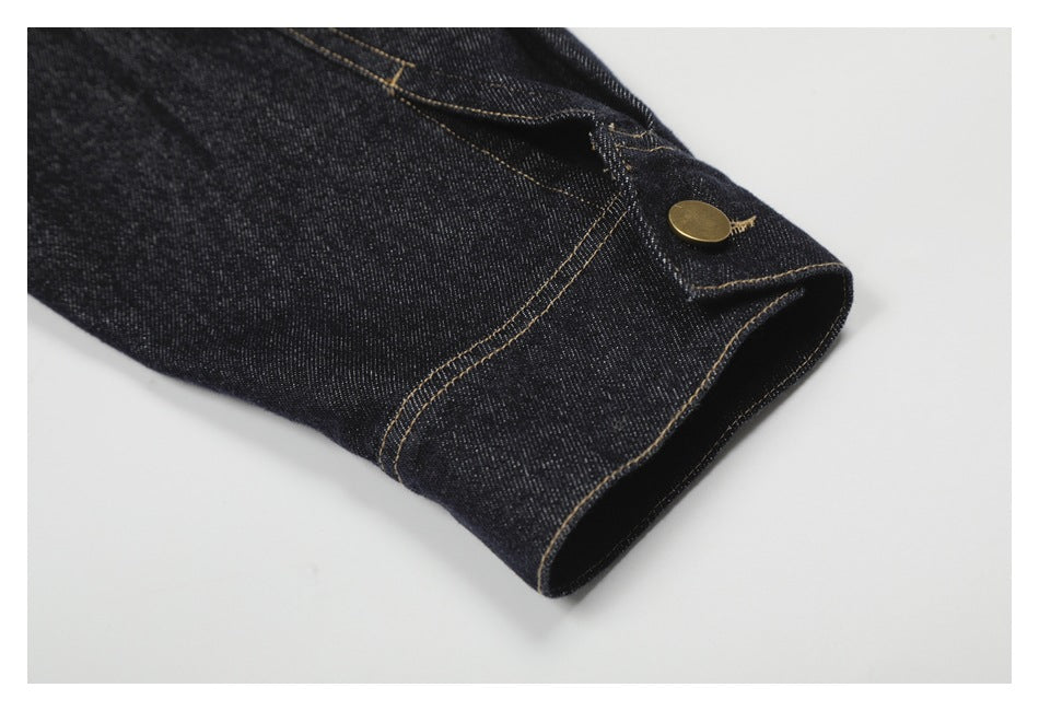 Close-up of a dark denim sleeve cuff with tan stitching and a brass button.