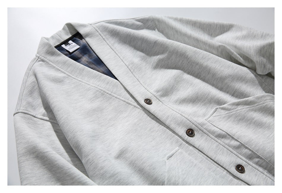 Angled front view of a light gray cardigan with a shawl collar, dark buttons, patch pockets, and blue plaid lining.