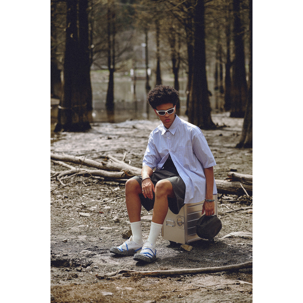 Seated model wearing an oversized pale blue pinstriped short-sleeve button-up shirt with a chest pocket.