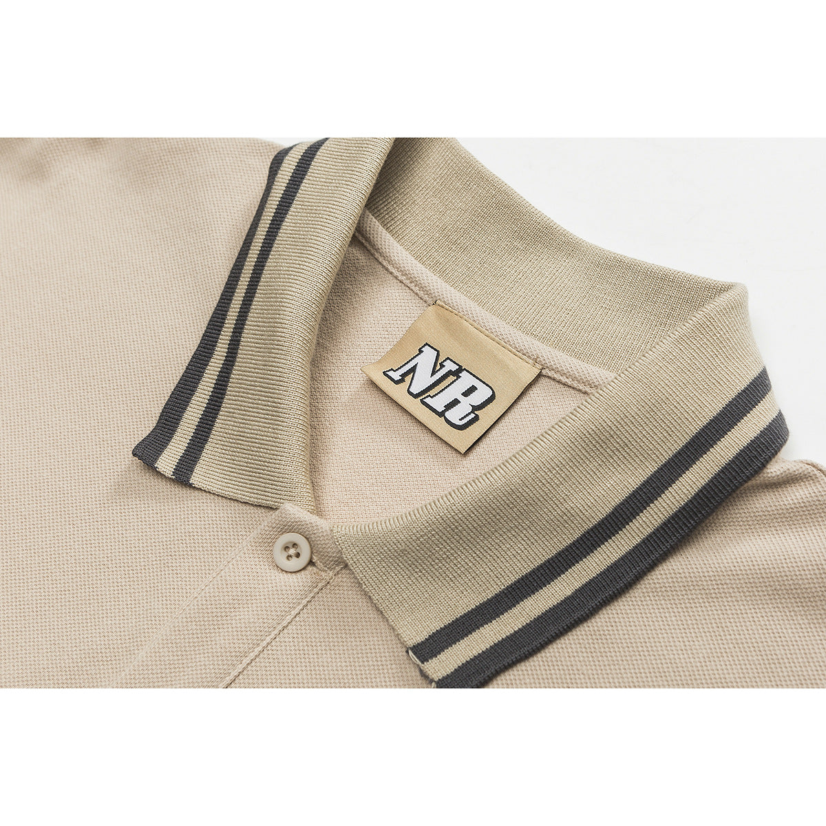 Close-up of a beige polo shirt collar with dark striped trim, a button, and a sewn NB neck label.