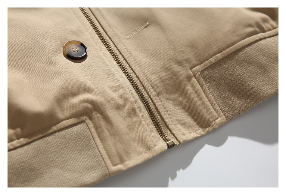 Close-up of a tan jacket's zipper, button, stitched pocket, and ribbed hem.