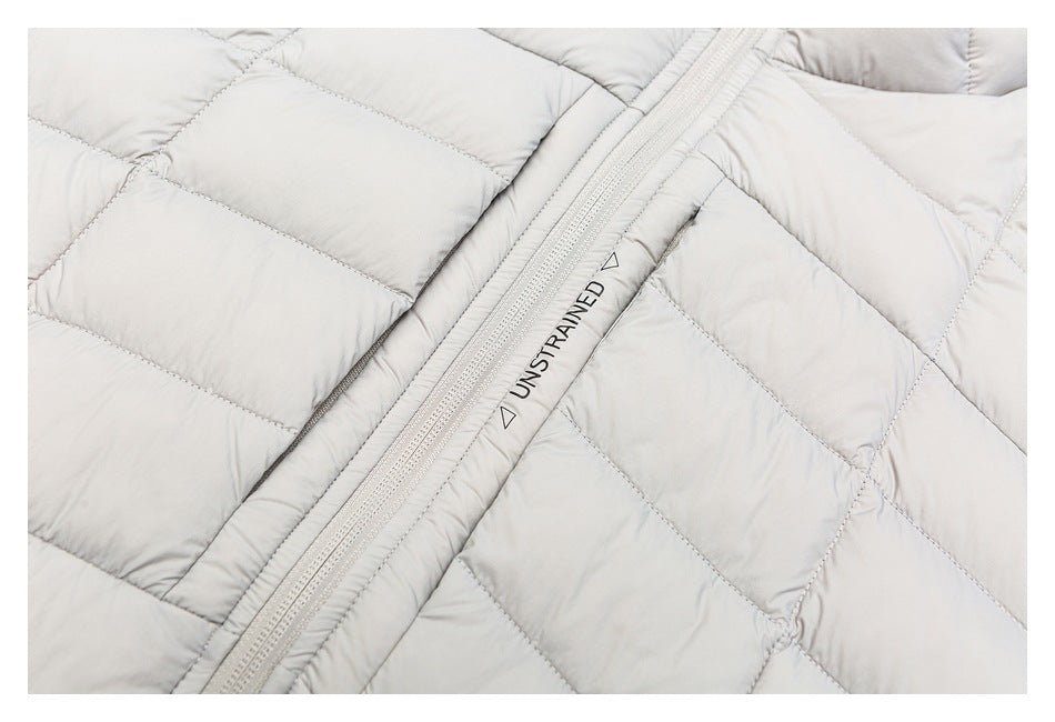 Close-up of a light gray quilted jacket with a front zipper and black UNSTRAINED lettering.