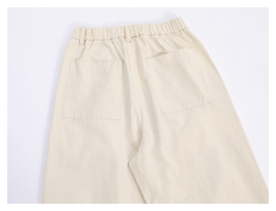 Back view of cream trousers laid flat, showing an elastic waist and two patch pockets.