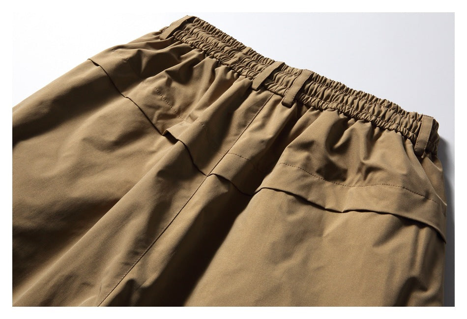 Close-up of brown trousers with a gathered elastic waistband, belt loops, and stitched front panels.