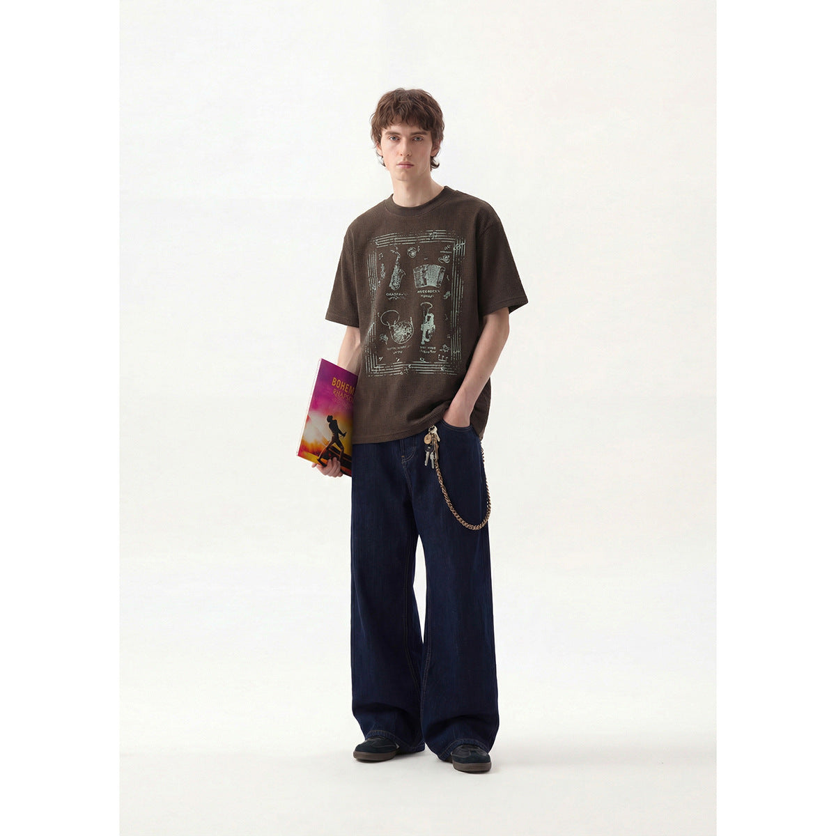 Model wearing a dark brown T-shirt with a large music-themed graphic, shown from the front.