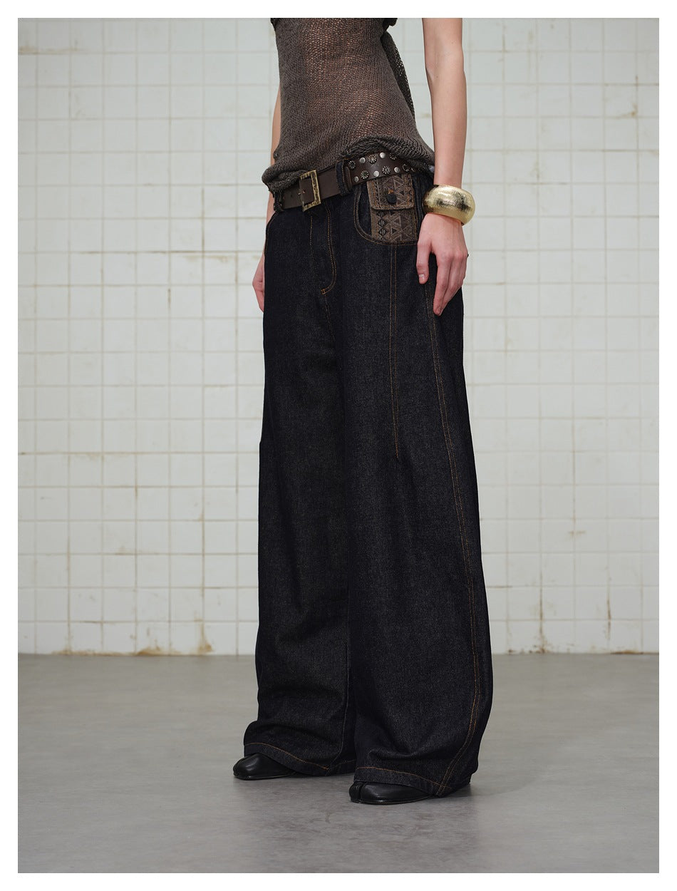 Cropped view of a model wearing dark, wide-leg jeans with contrast stitching and a patterned pocket detail.