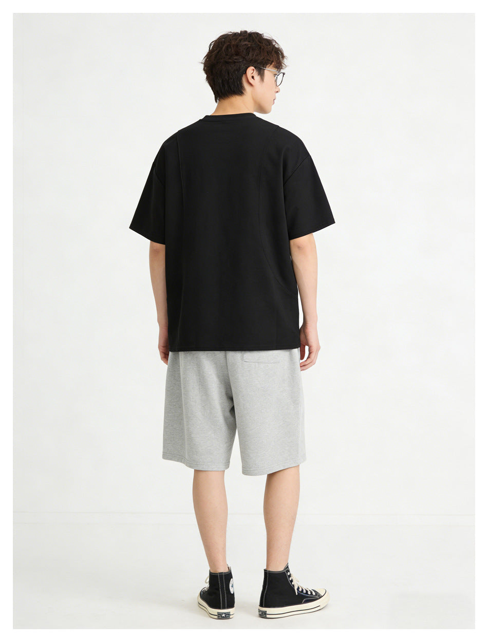 Model viewed from behind wearing a loose black short-sleeve T-shirt with light gray knee-length shorts.