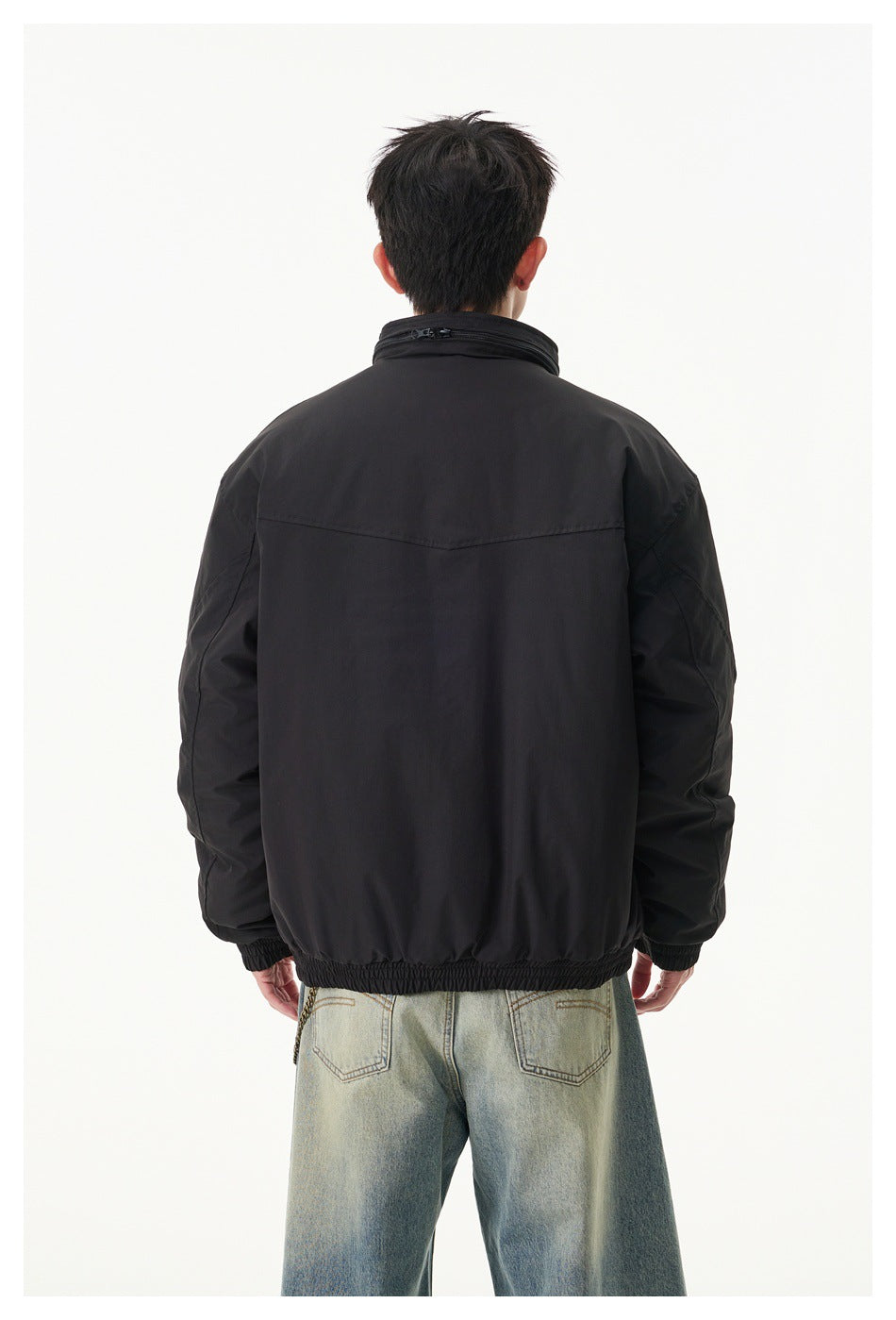 Back view of a model wearing a black zip-front jacket with a high collar, elastic cuffs and hem.