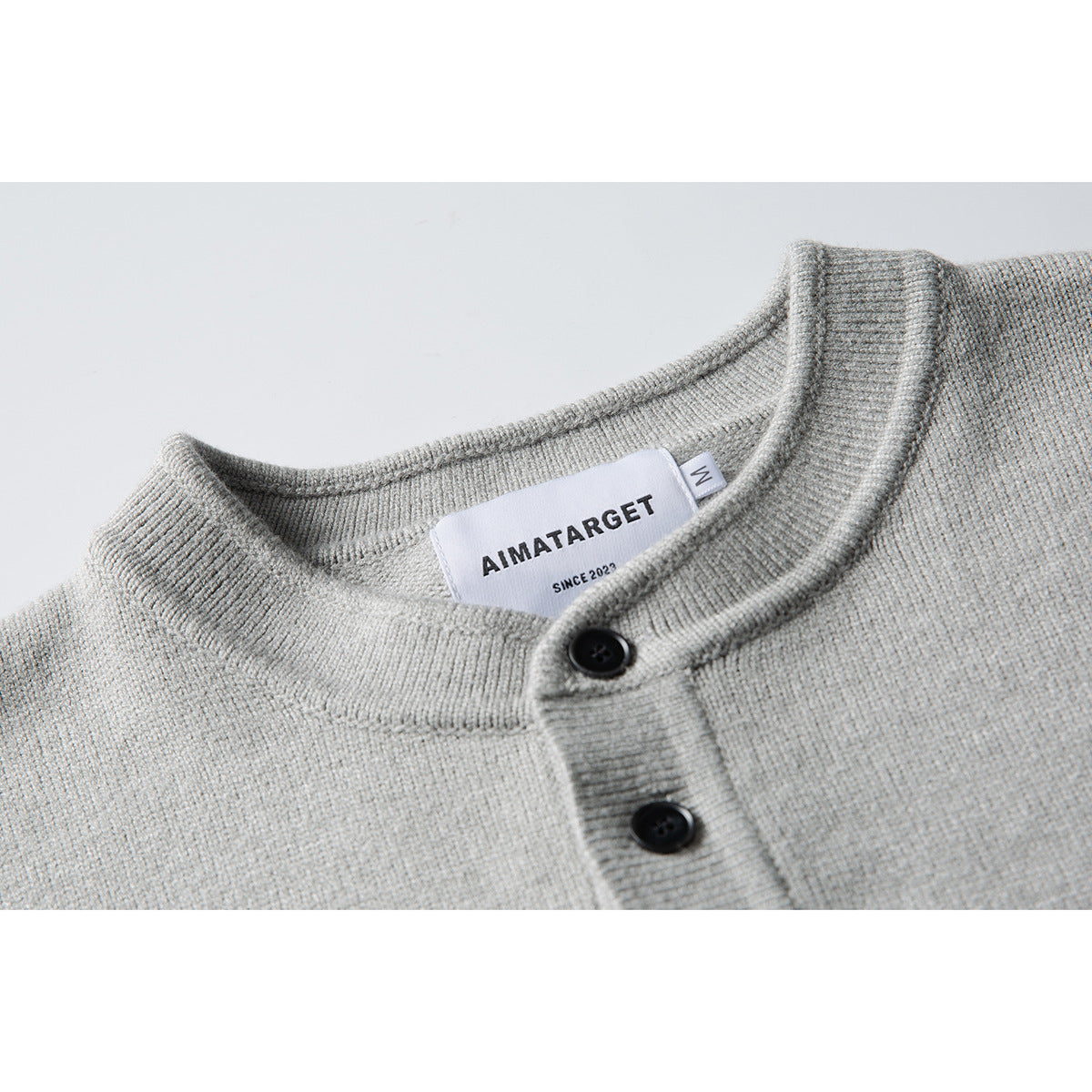 Close-up of a light gray knit sweater's ribbed band collar, black buttons and sewn neck label.