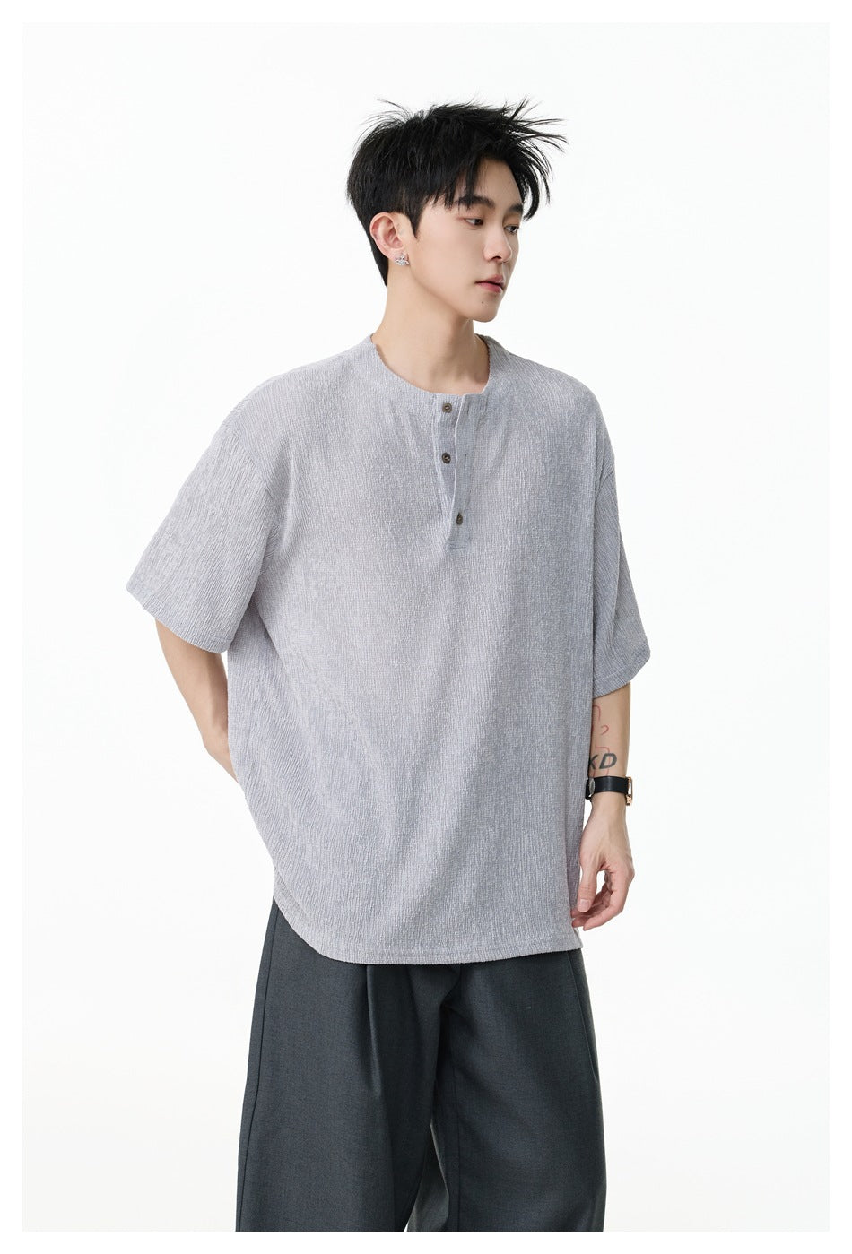 Model wearing a light gray oversized short-sleeve top with a three-button collar and dark wide-leg trousers.