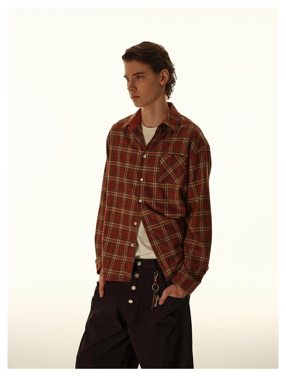 Model wearing a red plaid button-up shirt open over a white tee with dark wide trousers, three-quarter view
