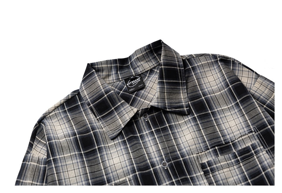 Cropped front view of a black, gray, and cream plaid button-up shirt with a pointed collar and chest pocket.