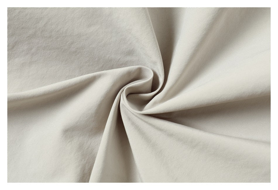 Close-up of light beige fabric gathered into a spiral, showing its smooth surface and folds.