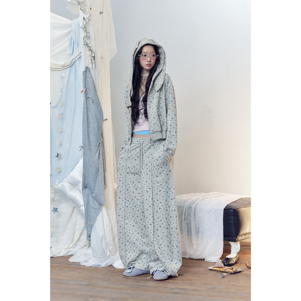 Model wearing a gray-blue floral zip hoodie and matching wide-leg pants, standing with the hood up.