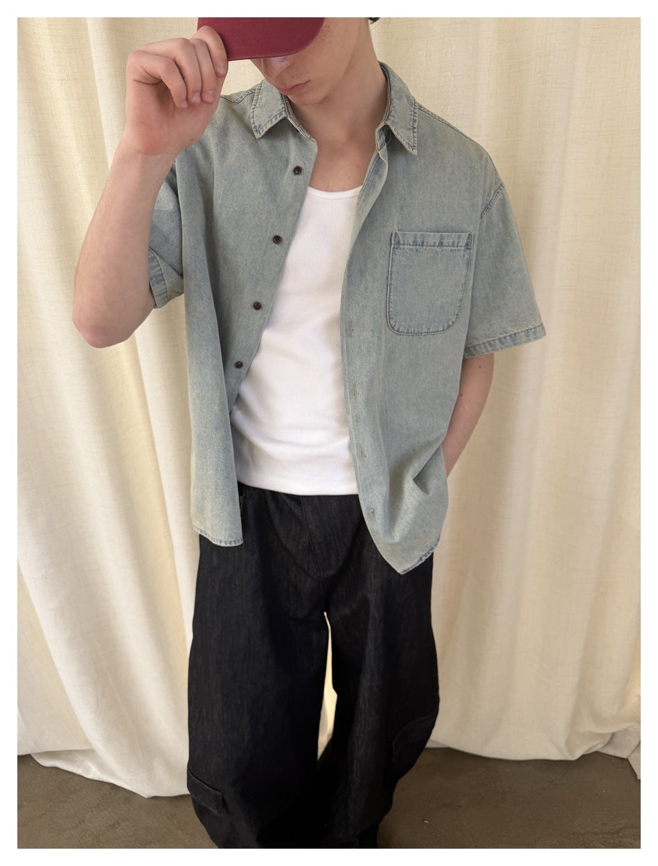 Close view of a light blue short-sleeve button-up shirt with a chest pocket, worn open over a white top.