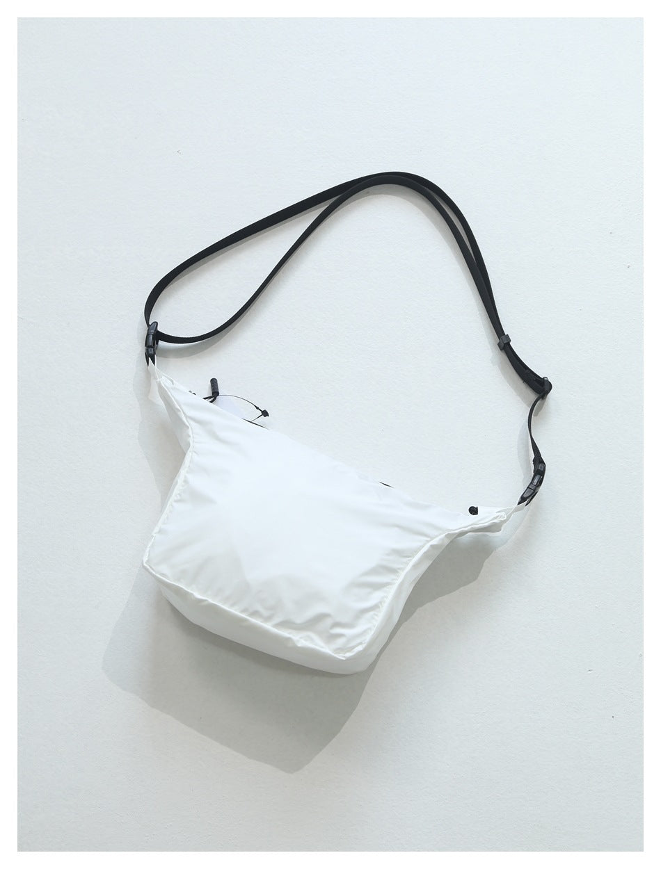 White crossbody bag with black strap and buckles, flat lay with soft shadow on a light surface