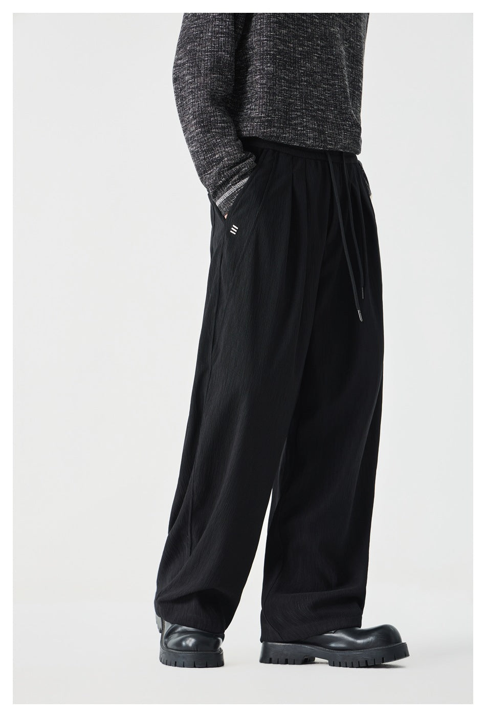 Angled view of black wide-leg drawstring pants worn with a dark sweater and black shoes.