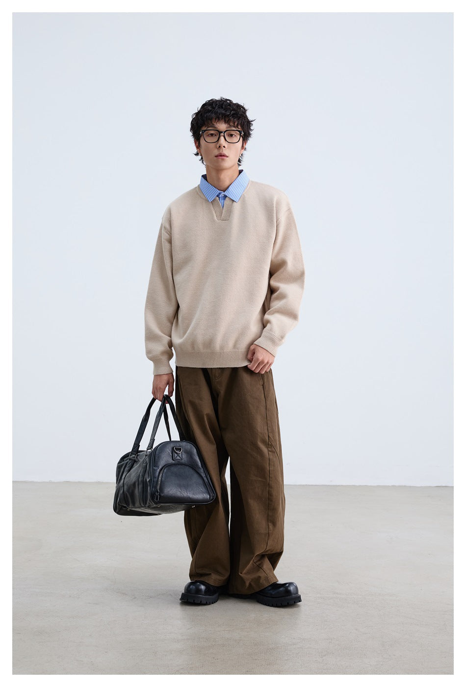 Full-length front view of a model wearing a relaxed beige V-neck sweater over a blue striped shirt.
