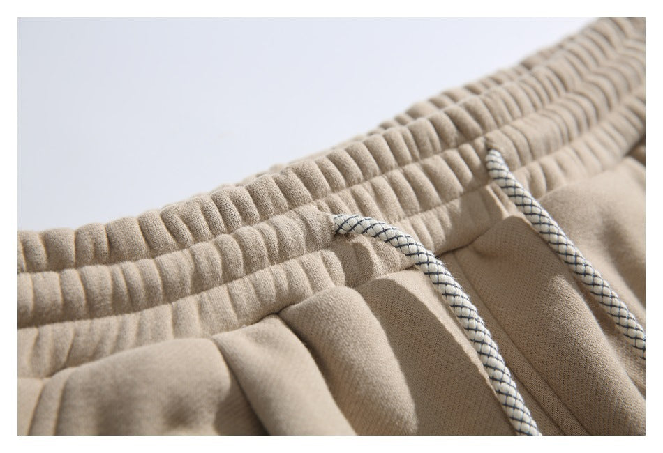 Close view of the gathered waistband and braided drawstrings on beige jogger pants.