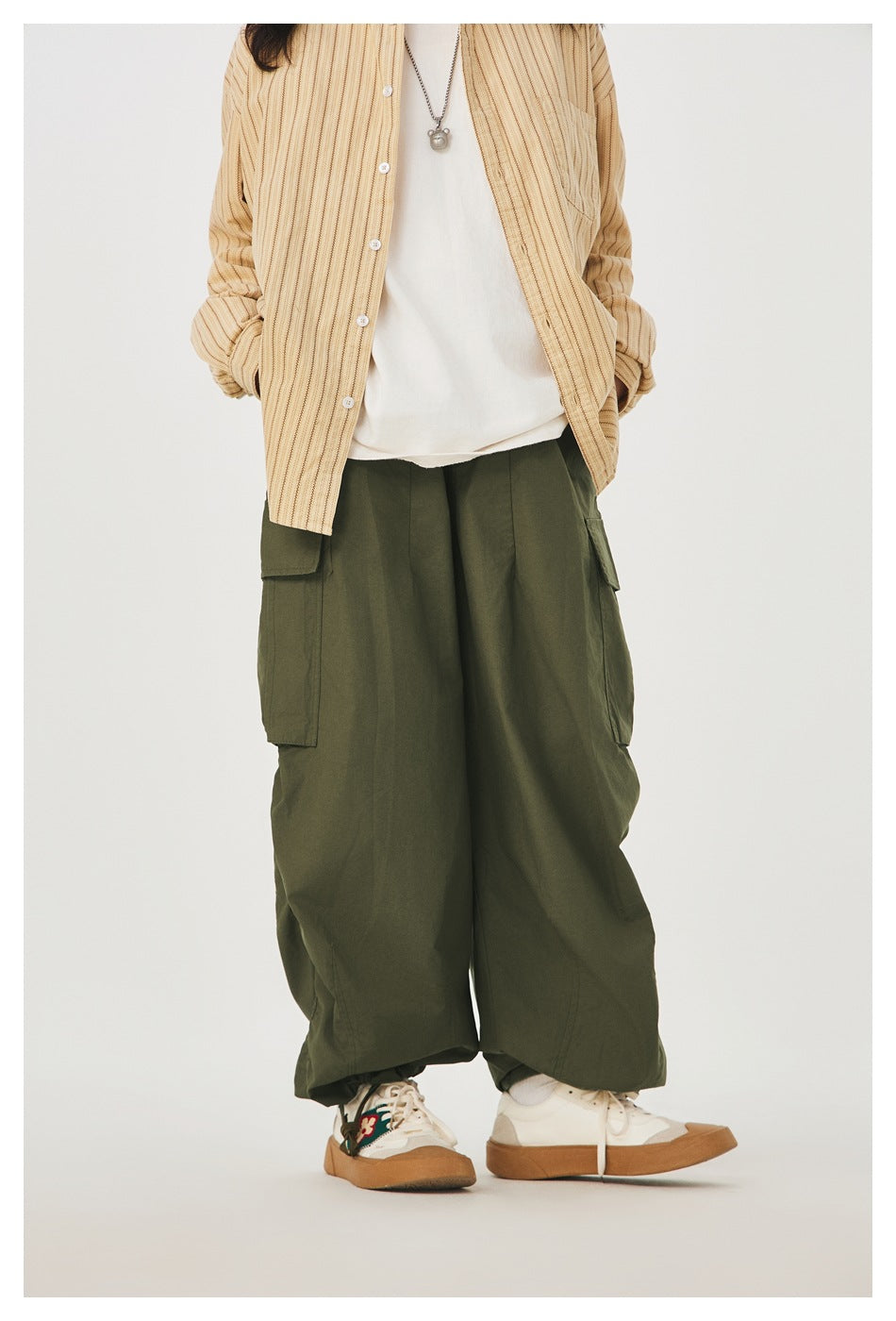 Cropped front view of a model wearing wide olive cargo pants with large side pockets and gathered hems.