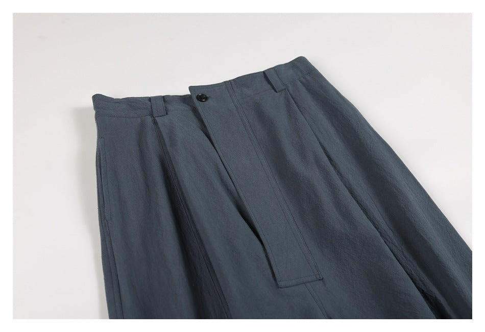Angled close-up of dark slate-blue trousers showing the waistband, buttoned fly, belt loops and side pocket.