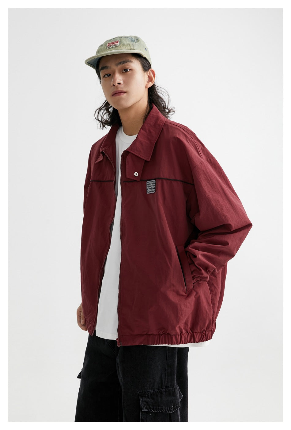 Three-quarter view of a model in an open burgundy jacket with a pointed collar, black chest trim and patch.