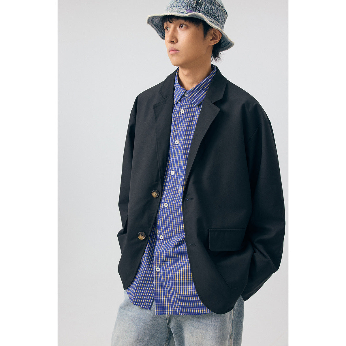 Front view of a model wearing an oversized black blazer with a blue checked shirt and light jeans.