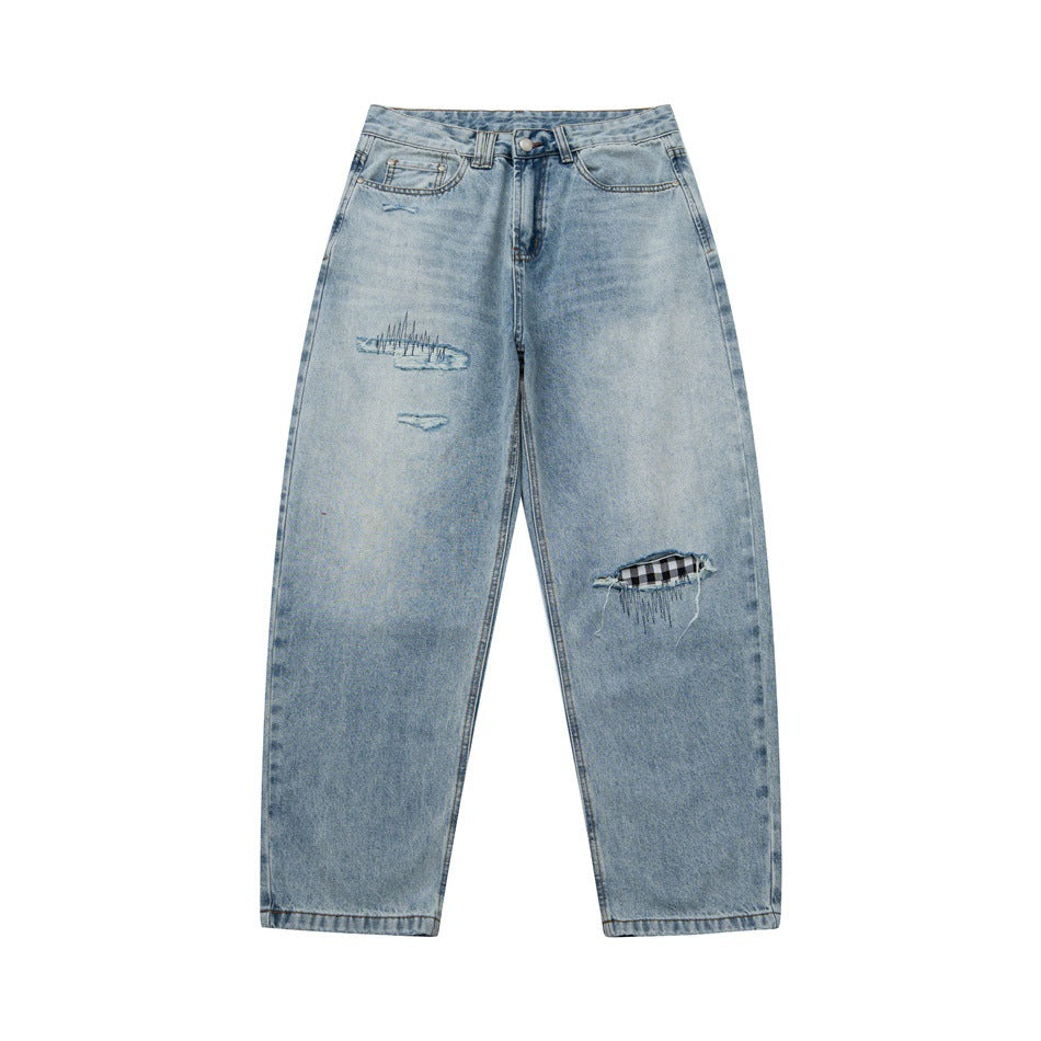 Front of light blue faded jeans with distressed rips, embroidered stitching and gingham fabric behind the knee rip