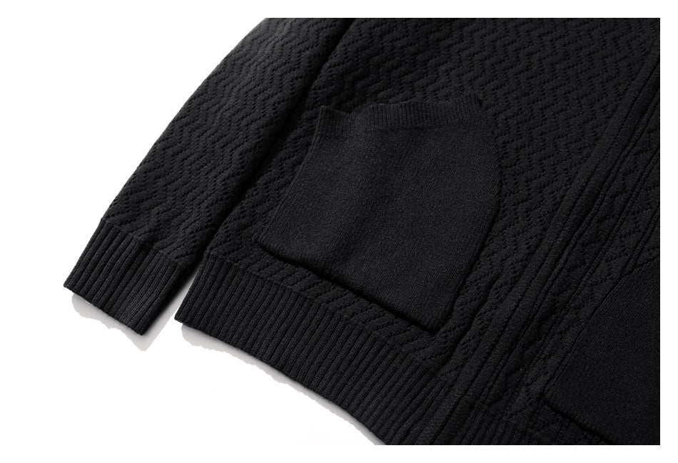 Close-up of a black textured knit sweater showing its large front pocket, ribbed hem, and sleeve cuff.