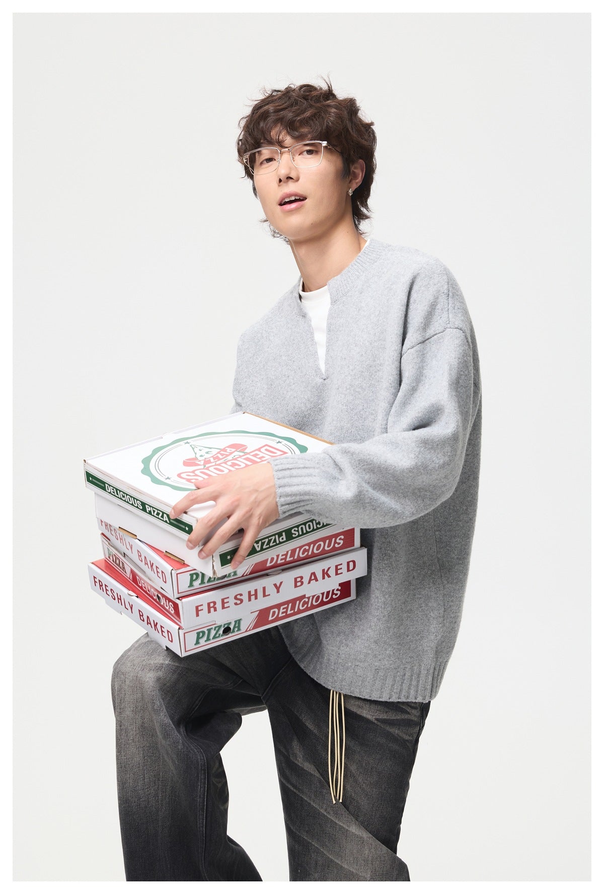 Model wearing a light gray oversized split-neck sweater while holding stacked pizza boxes.