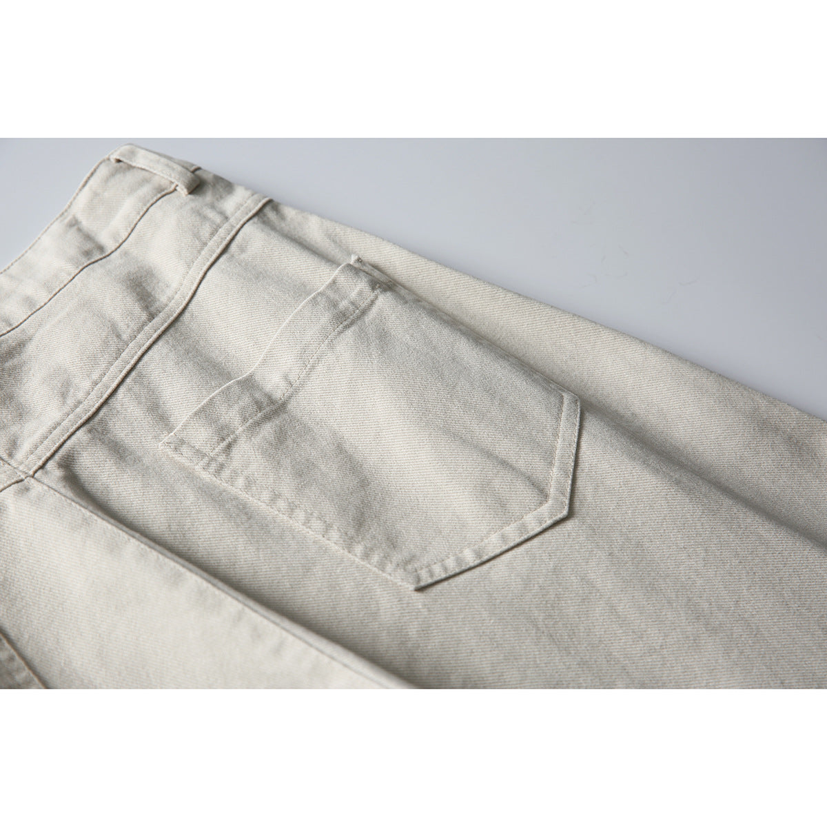 Close-up of the back of light beige trousers, highlighting a single angular patch pocket and waistband.