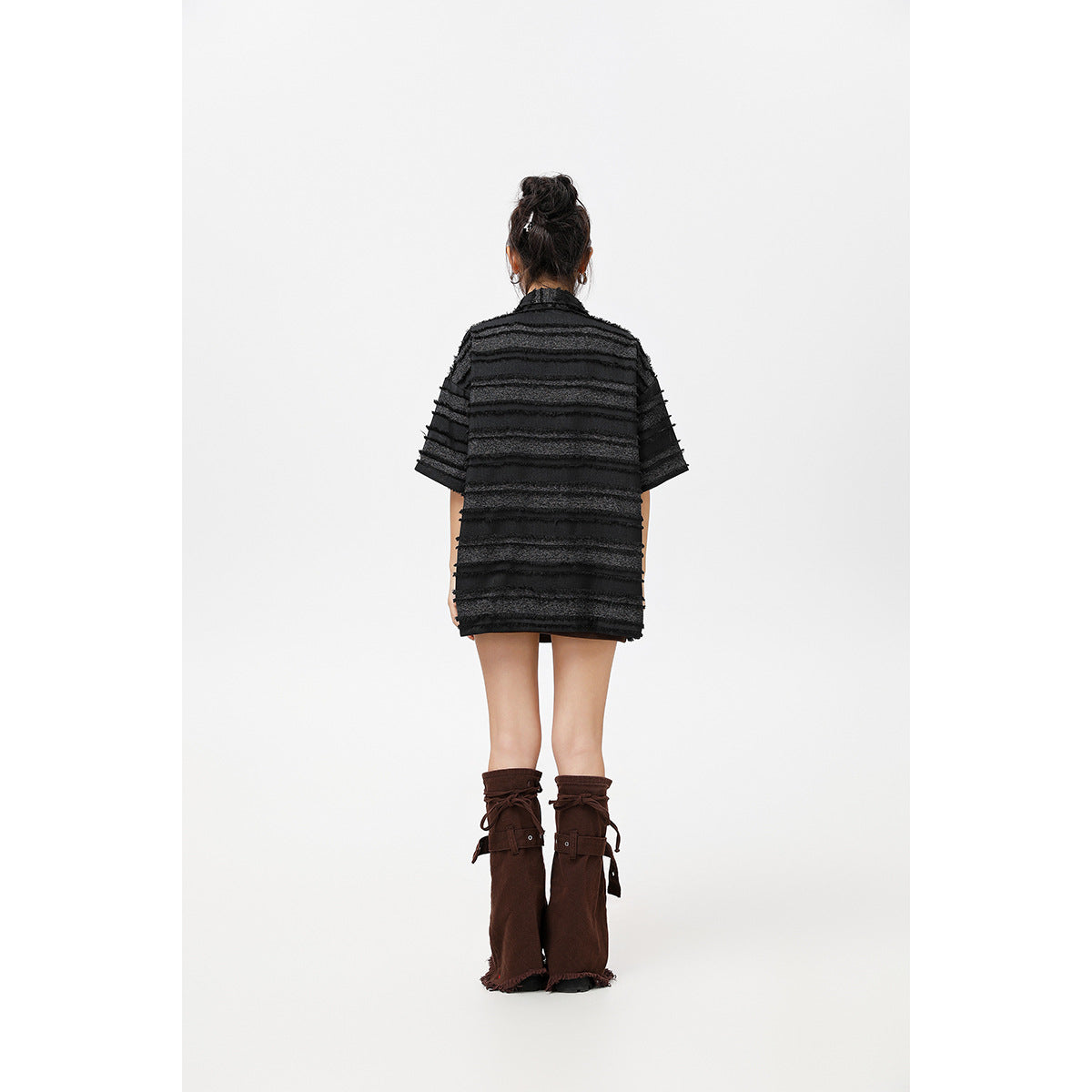 Back view of a model wearing an oversized black horizontally striped short-sleeve shirt and tall brown boots.
