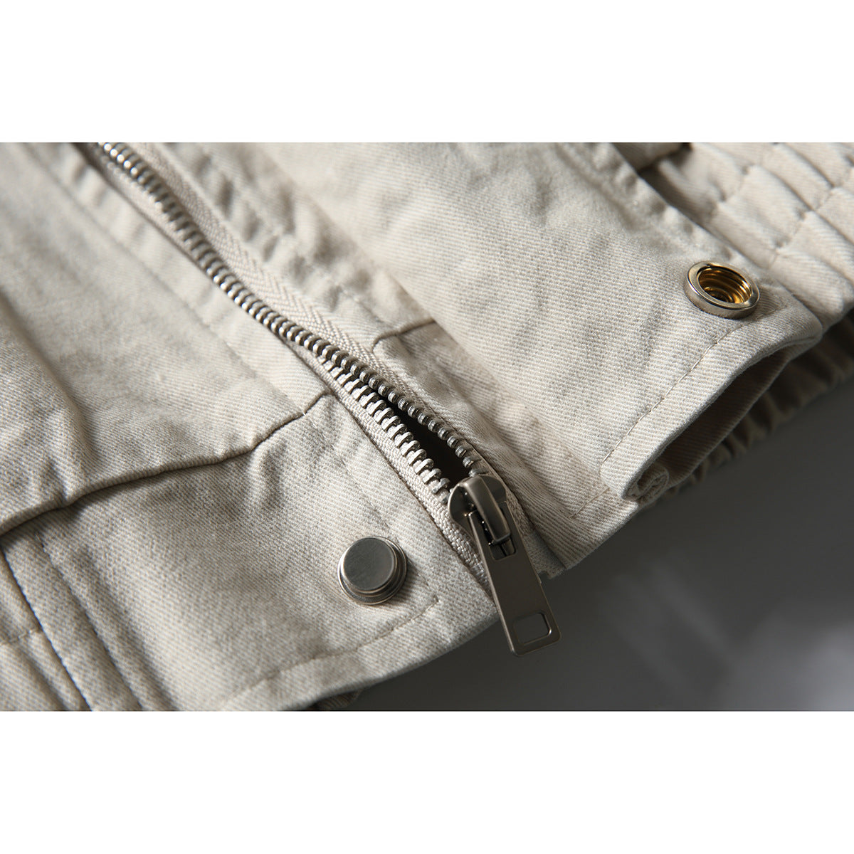Close-up of an off-white jacket zipper, metal snaps, and fabric eyelet.