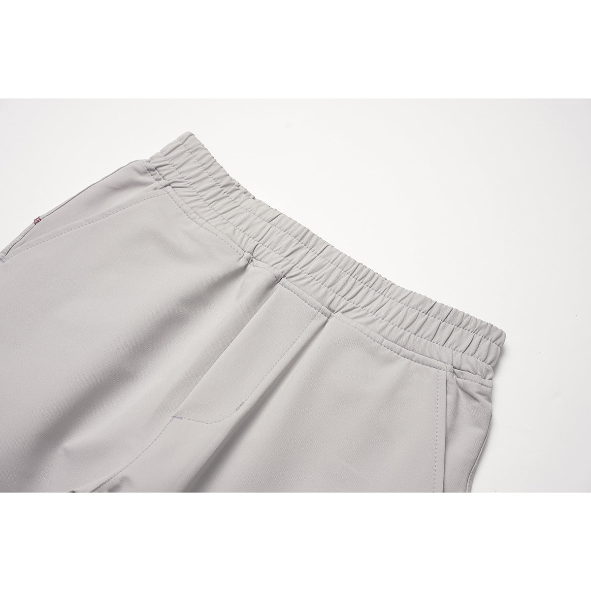 Close-up of light gray pants showing the gathered elastic waistband, drawstring, and front pocket seams.