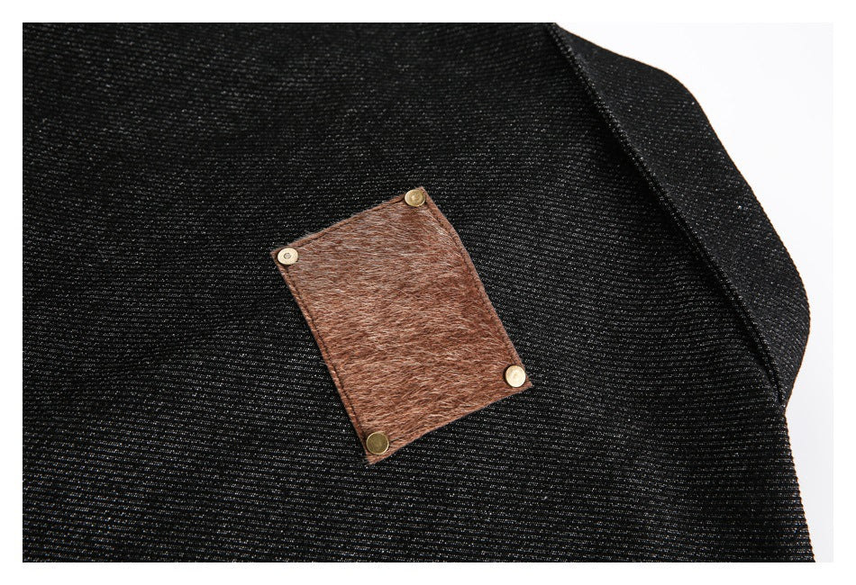 Close-up of black denim with a rectangular brown leather patch secured by metal rivets.