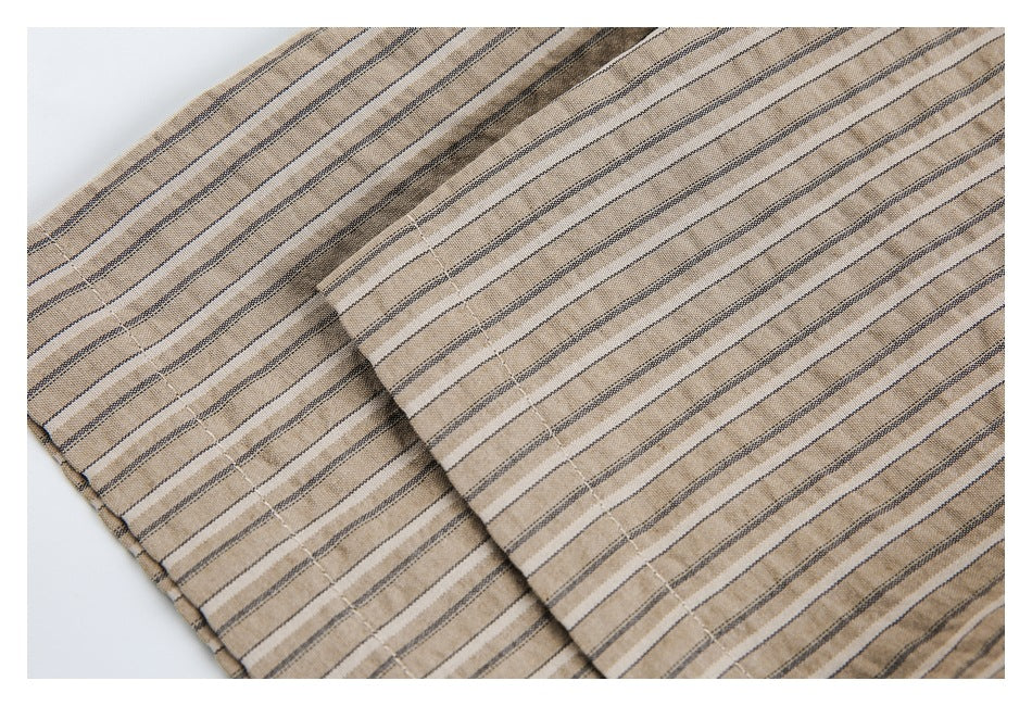 Close-up of tan shirt fabric with narrow dark stripes and a stitched seam.
