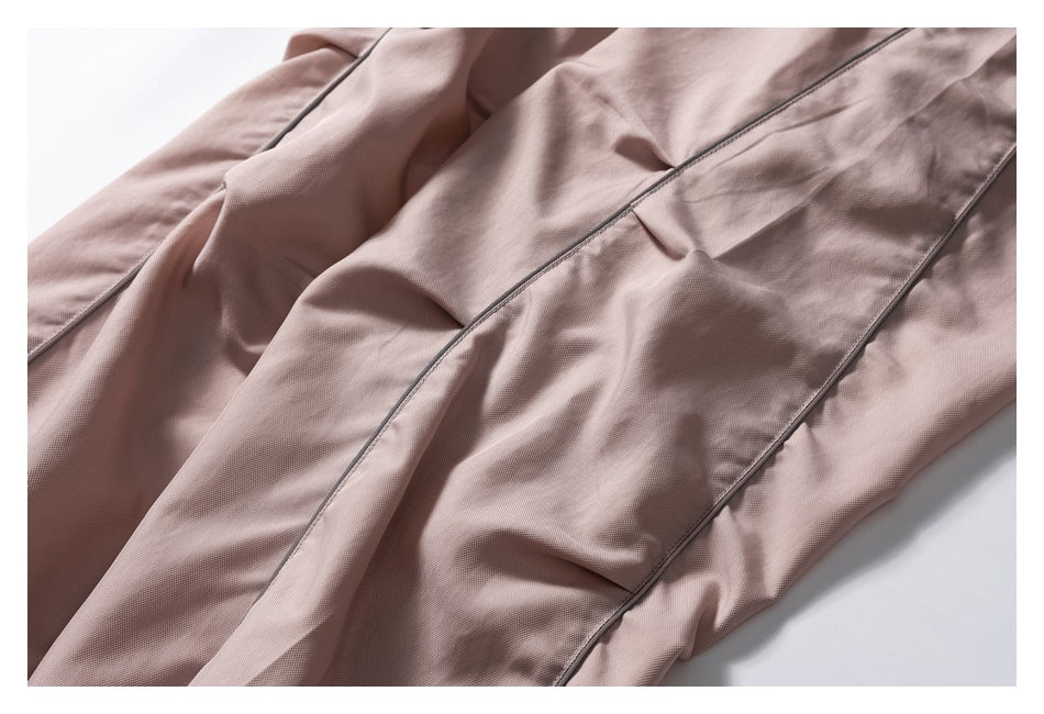 Close-up of dusty rose trouser fabric with dark piping along the seams.