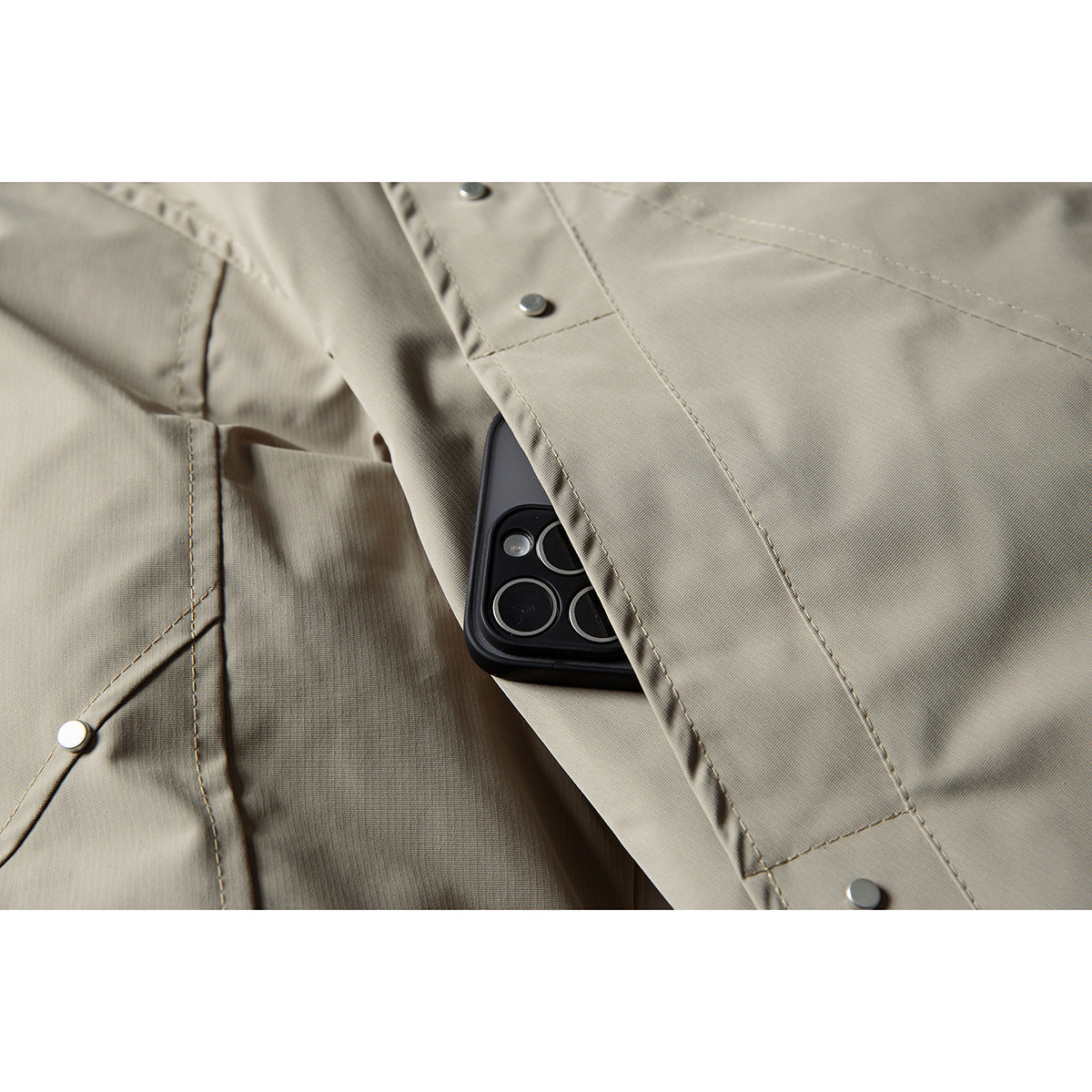 Close-up of a taupe jacket's snap-fastened pocket with a black phone tucked inside.